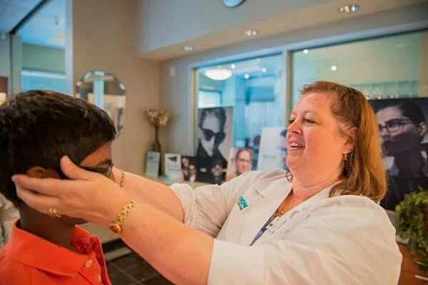 a medical assistant helps fit a young patient with new glasses