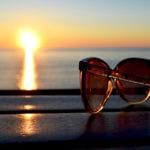 A pair of sunglasses sitting on table at the ocean shore during sunset.