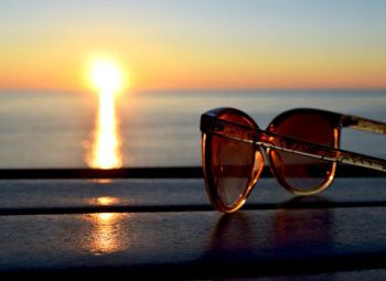 A pair of sunglasses sitting on table at the ocean shore during sunset.