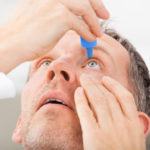 Middle aged man putting eye drops into his eyes, and facing upwards.