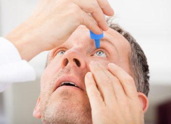 Middle aged man putting eye drops into his eyes, and facing upwards.