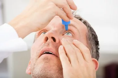 Middle aged man putting eye drops into his eyes, and facing upwards.