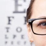 Woman with glasses standing in front of Snellen eye chart.