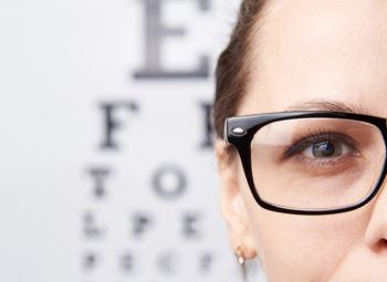 Woman with glasses standing in front of Snellen eye chart.