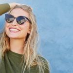 blonde woman looking up and brushing back hair with sunglasses on