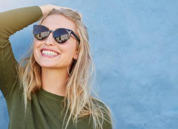 blonde woman looking up and brushing back hair with sunglasses on