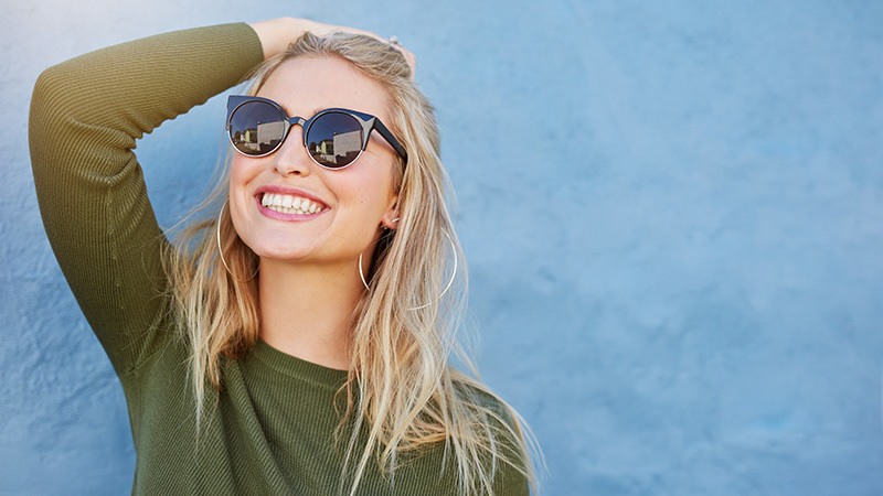 blonde woman looking up and brushing back hair with sunglasses on