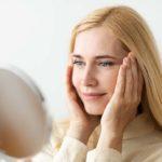 Mature Woman Looking At Mirror And Touching Face