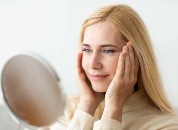 Mature Woman Looking At Mirror And Touching Face