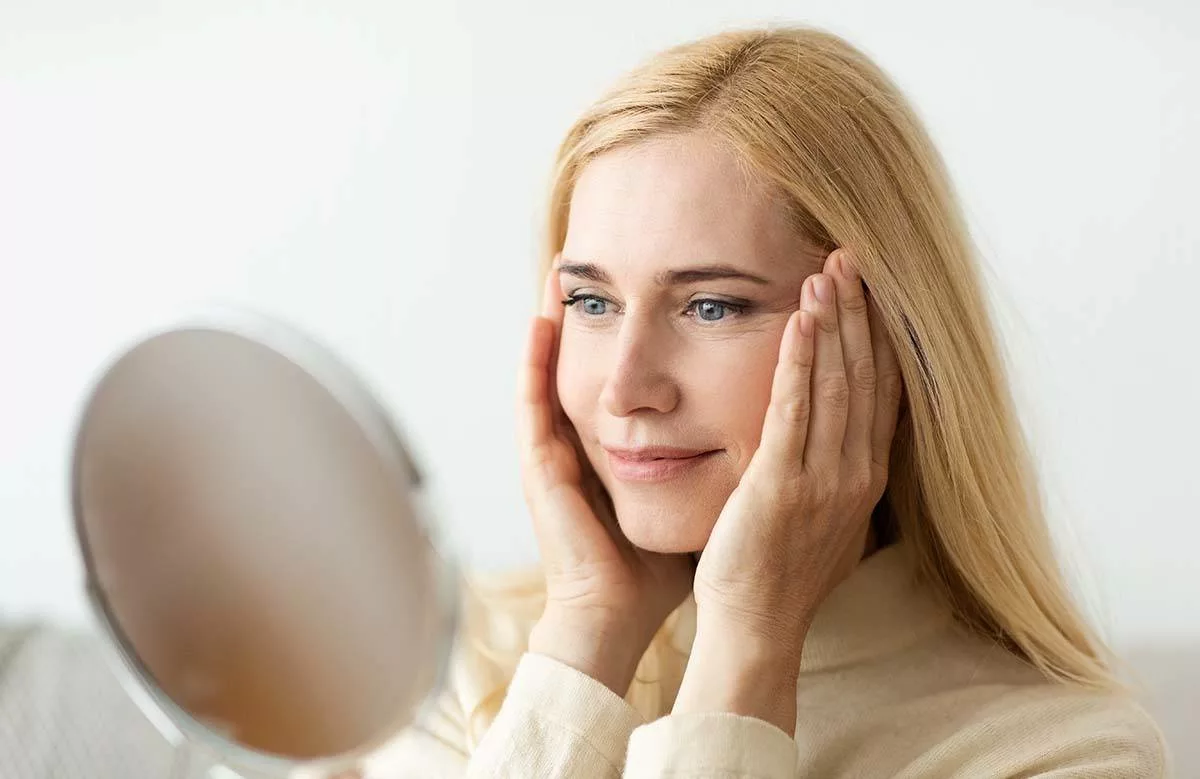 Mature Woman Looking At Mirror And Touching Face