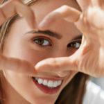 young women smiling and holding her hand in a heart shape around her eye