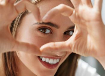 young women smiling and holding her hand in a heart shape around her eye