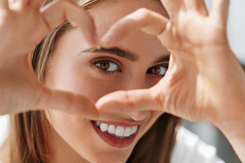 young women smiling and holding her hand in a heart shape around her eye