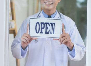 Doctor with Open sign welcoming patients into the clinic