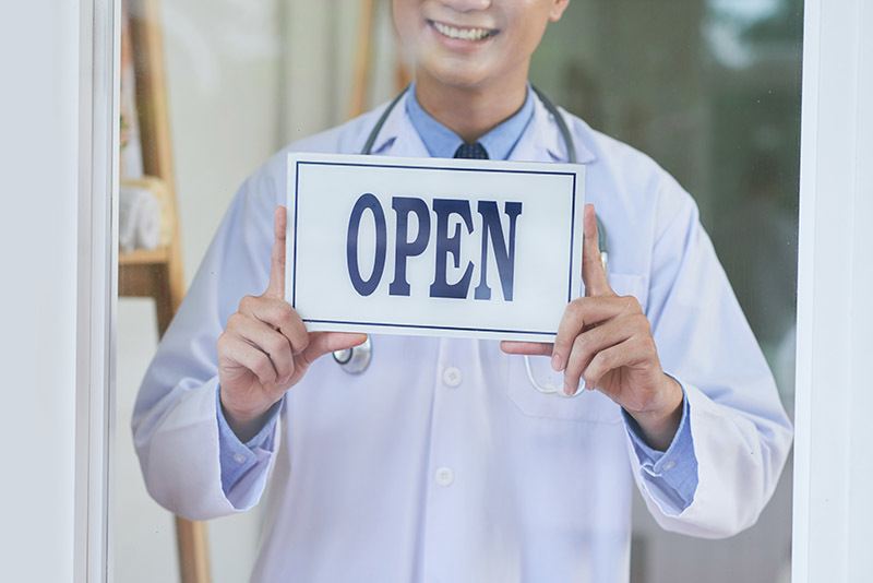 Doctor with Open sign welcoming patients into the clinic