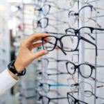 Row of glasses at an opticians. Eyeglasses shop. Stand with glasses in the store of optics. Woman chooses spectacles. Eyesight correction.