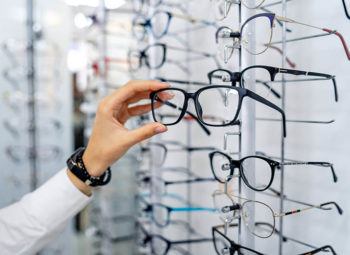 Row of glasses at an opticians. Eyeglasses shop. Stand with glasses in the store of optics. Woman chooses spectacles. Eyesight correction.