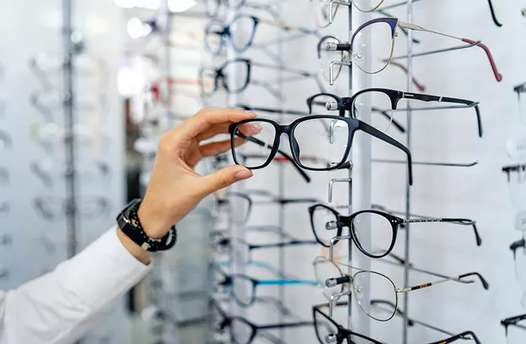 Row of glasses at an opticians. Eyeglasses shop. Stand with glasses in the store of optics. Woman chooses spectacles. Eyesight correction.