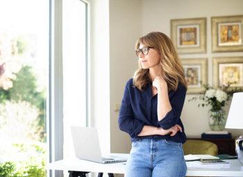 Women standing in home office wearing eyeglasses and looking thoughtful