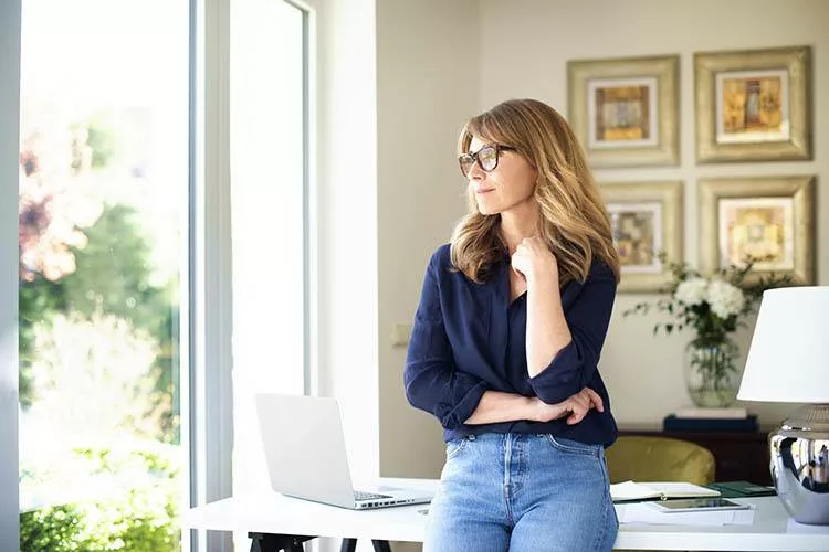 Women standing in home office wearing eyeglasses and looking thoughtful