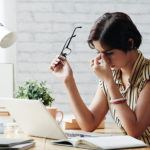 women with eyeglasses sitting at work desk rubbing her eyes