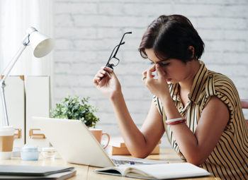 women with eyeglasses sitting at work desk rubbing her eyes