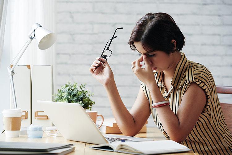 women with eyeglasses sitting at work desk rubbing her eyes