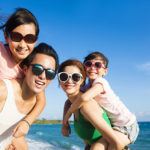 Happy Family of four wearing UV protective sunglasses and Having Fun at the Beach