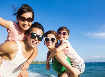 Happy Family of four wearing UV protective sunglasses and Having Fun at the Beach