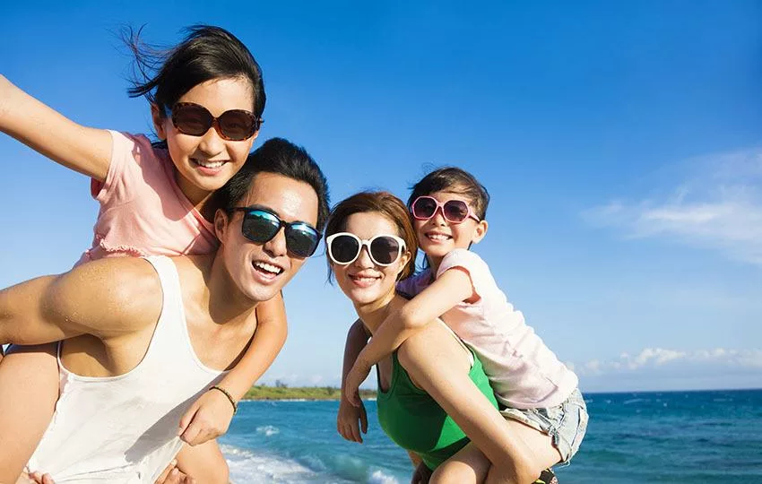 Happy Family of four wearing UV protective sunglasses and Having Fun at the Beach