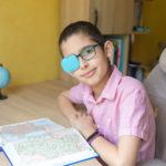 Young boy in glasses with eye patch covering one lens as treatment for lazy eye (amblyopia)