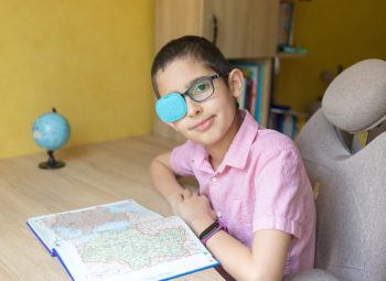 Young boy in glasses with eye patch covering one lens as treatment for lazy eye (amblyopia)