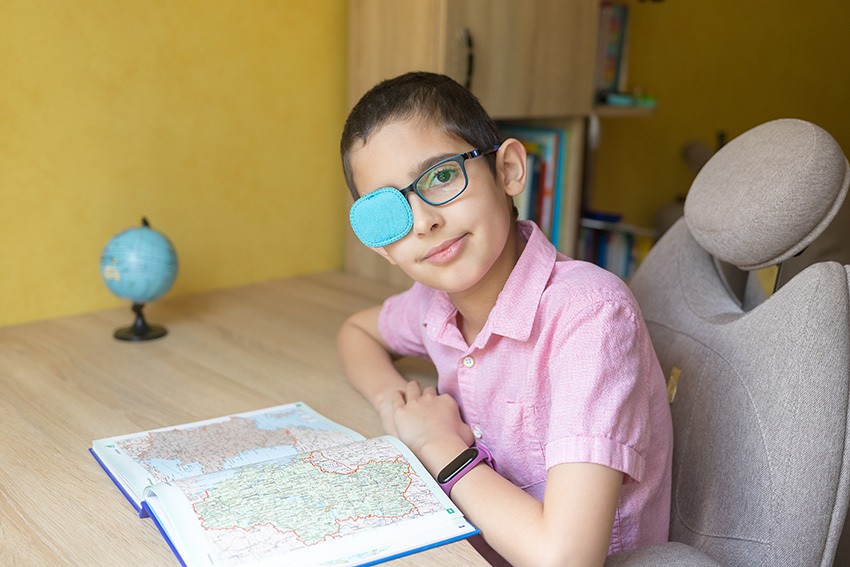 Young boy in glasses with eye patch covering one lens as treatment for lazy eye (amblyopia)
