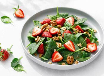strawberry spinach and walnut salad in white bowl with ingredients also scattered nearby