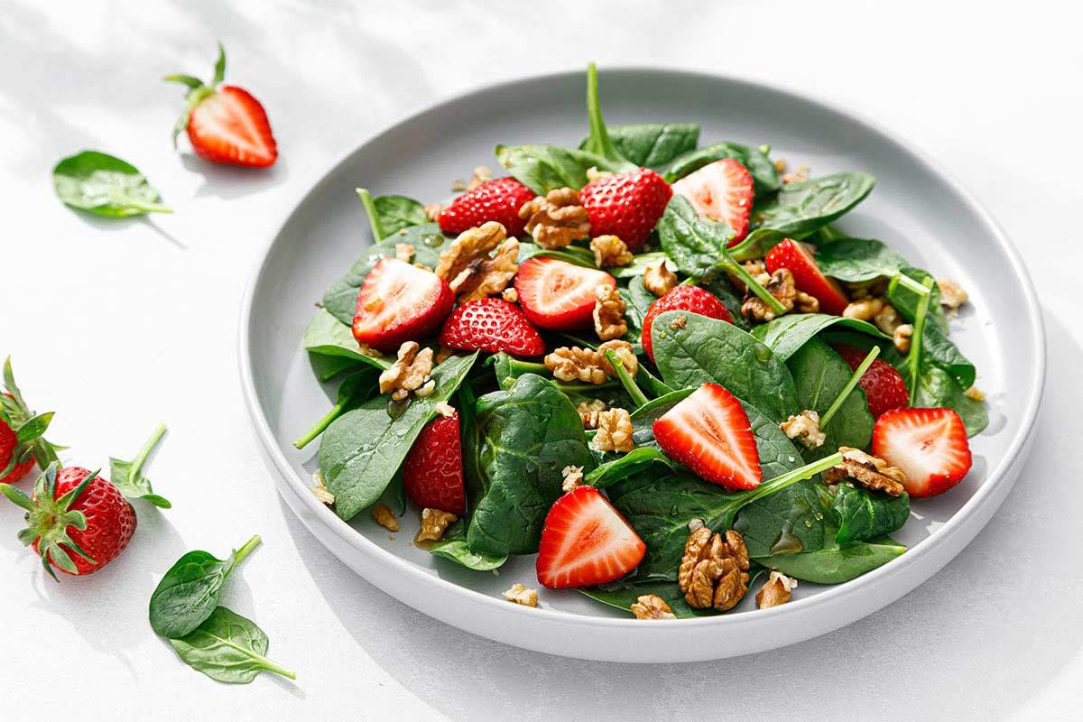 strawberry spinach and walnut salad in white bowl with ingredients also scattered nearby