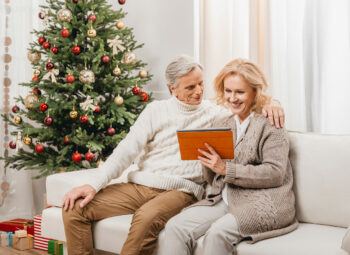 senior couple on couch by Christmas tree, looking at a tablet