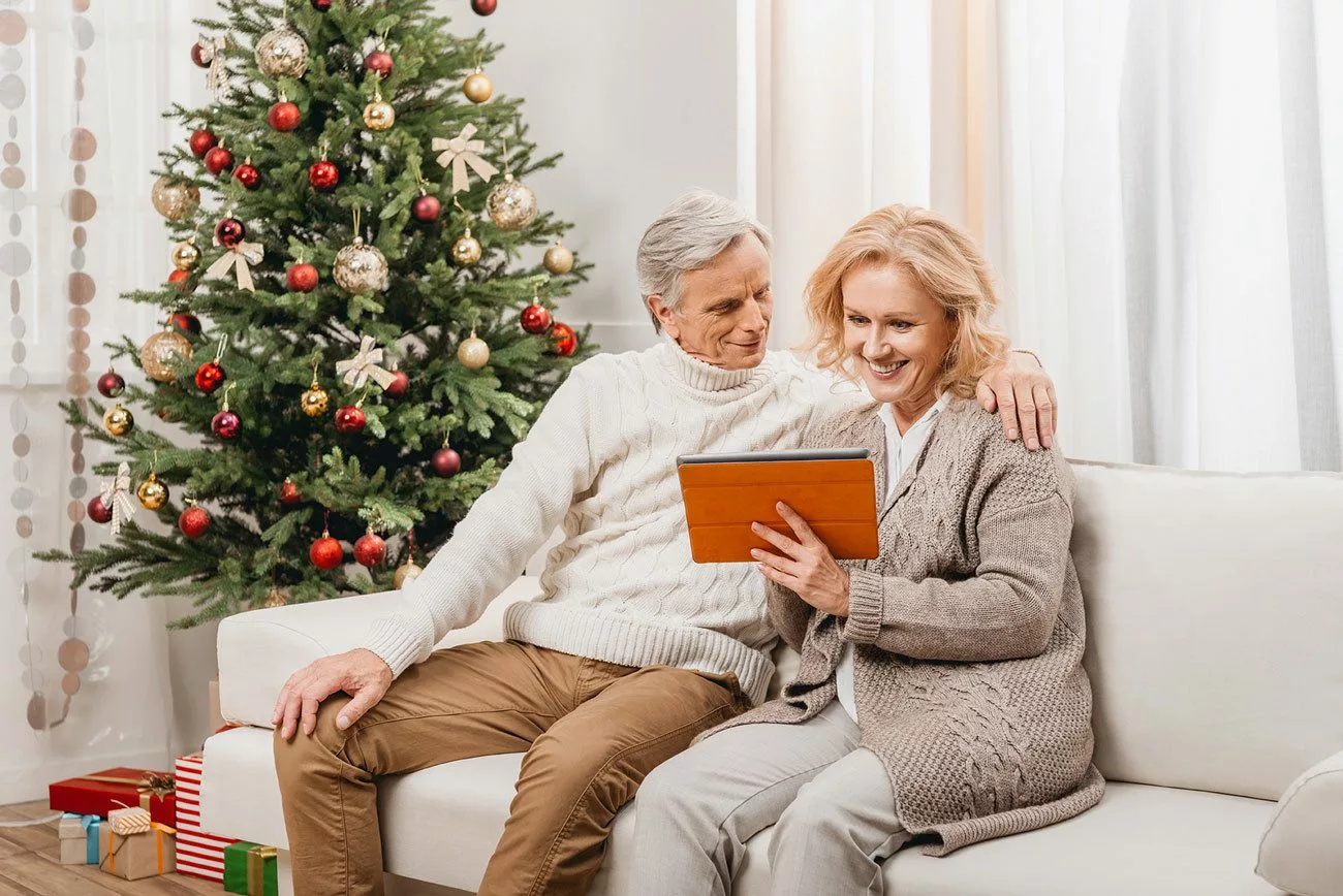 senior couple on couch by Christmas tree, looking at a tablet