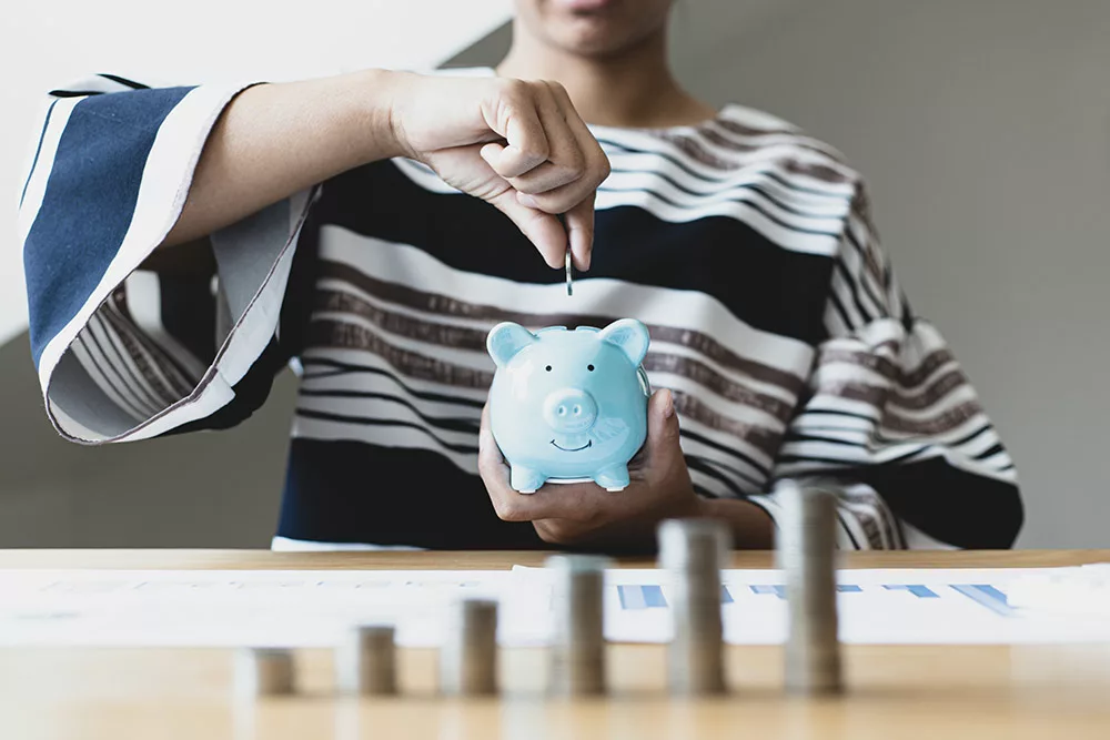 woman holding piggy bank in one hand while dropping coin into it with the other