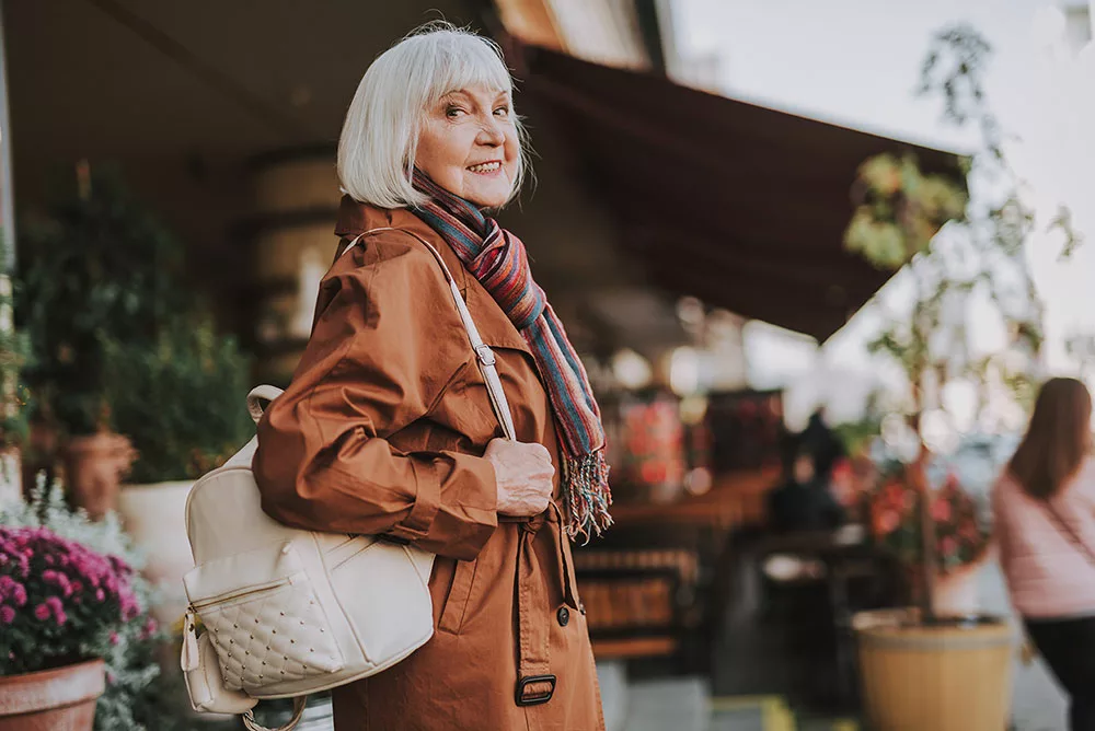Senior woman smiling over her shoulder while out walking wearing trenchcoat and carrying handbag
