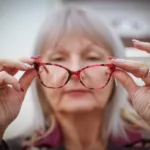 Senior woman holding glasses out from her face.