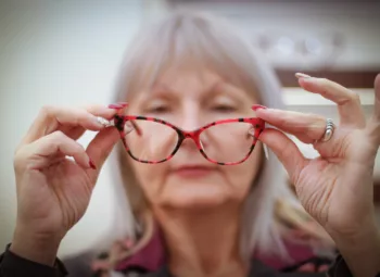 Senior woman holding glasses out from her face.