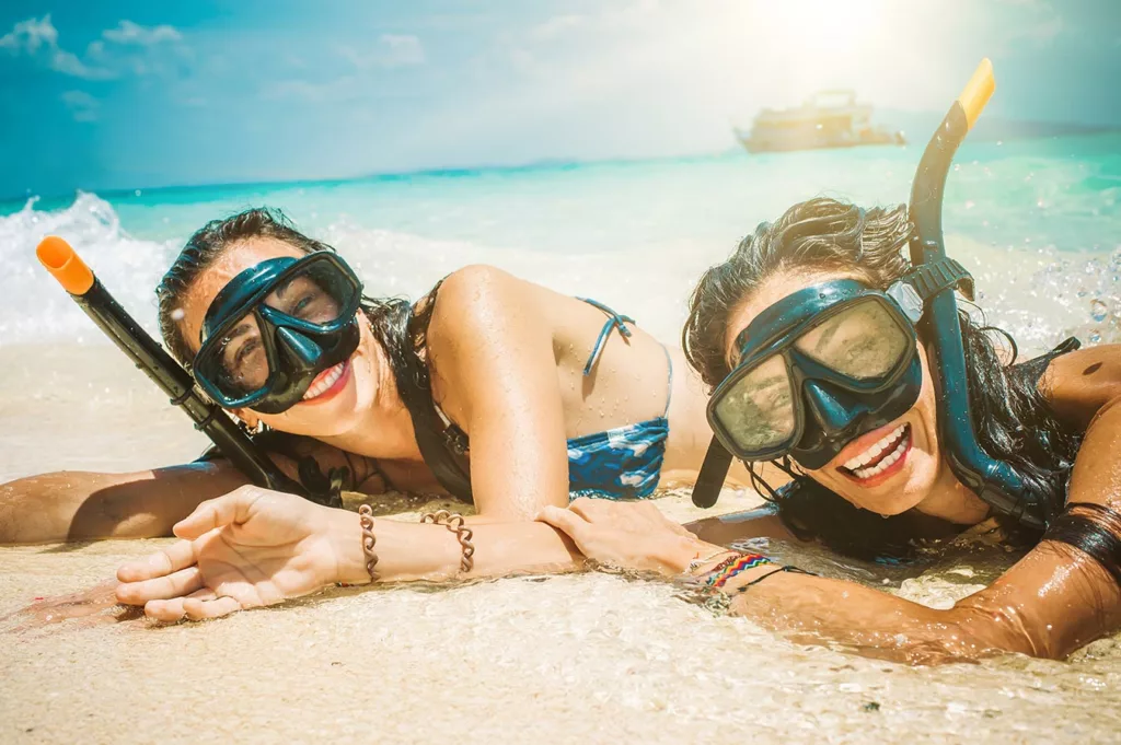Two woman lying in surf with snorkeling goggles on and smiling. 
