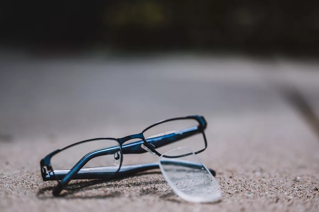 close-up of broken pair of glasses with lens popped out on pavement. 