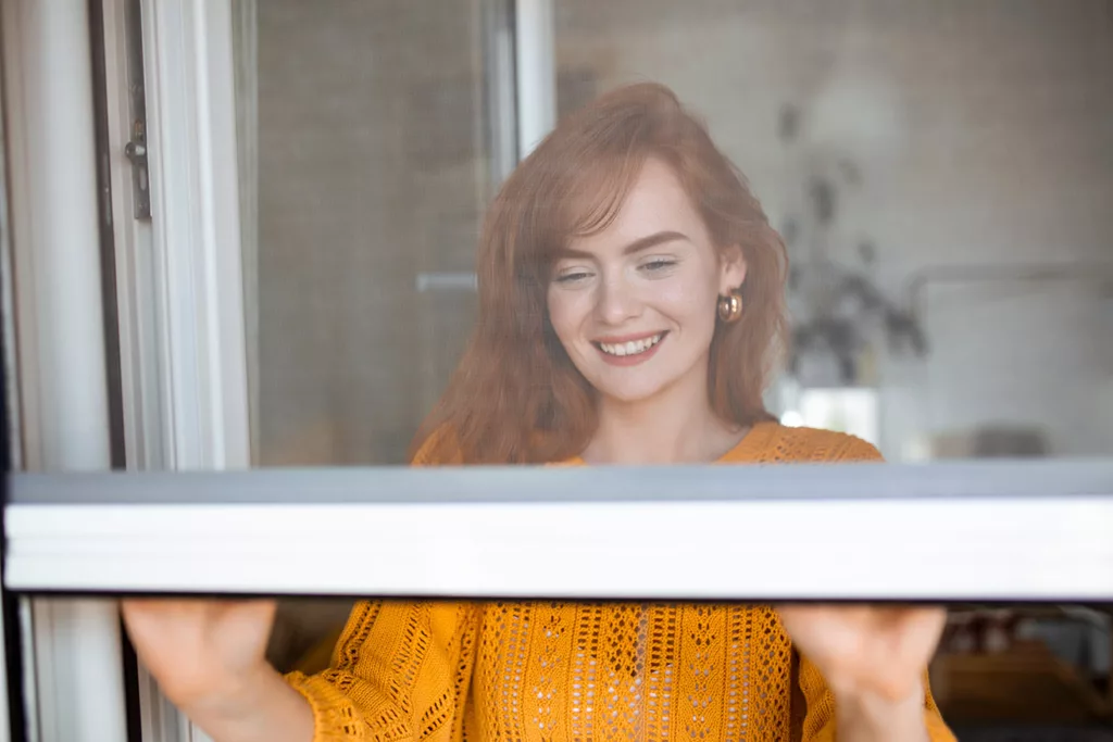 smiling, redheaded woman closing a window. 