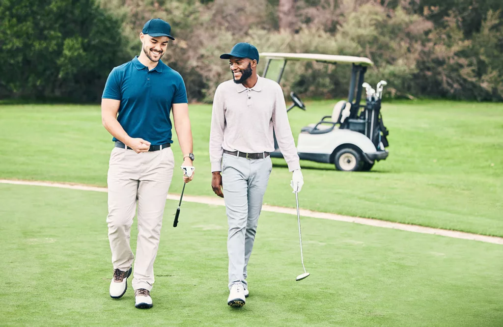 Two smiling professional golfers walk through a golf course with clear vision from LASIK eye surgery.