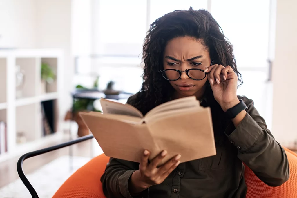 Woman with glasses and a book squints to read