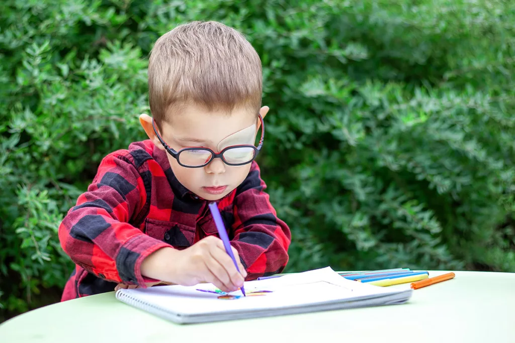 A child with ablyopia, or lazy eye, draws on a piece of paper in a garden.
