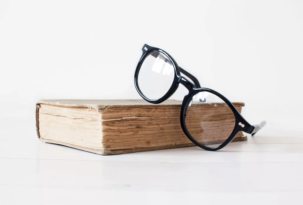 A pair of black eye glasses sits on top of an old book against a white background.