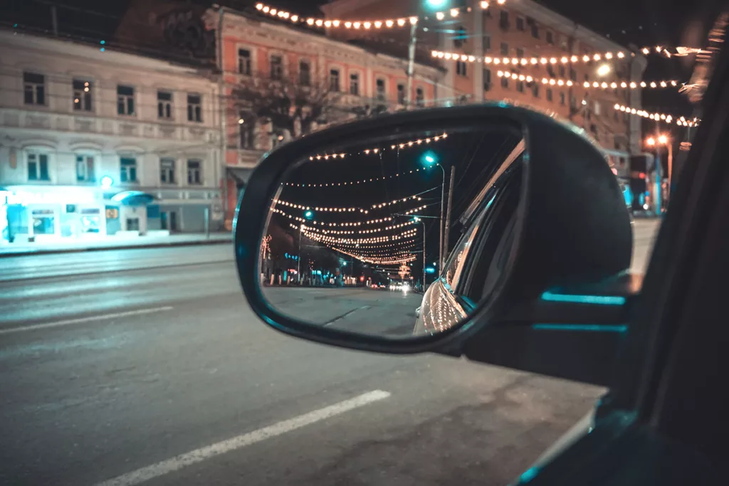 A car's rear view mirror reflects lights that are blurry from driving at night with cataracts.