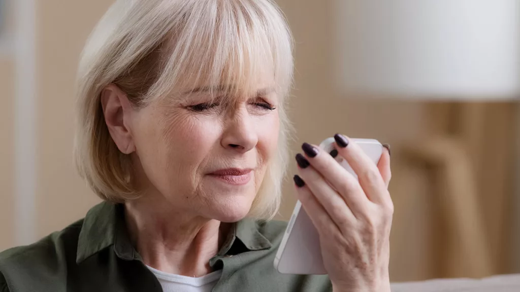 A woman with cataracts holds a phone, squinting to read due to blurry and cloudy vision.